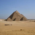 Camel caravan passing in front of the Giza pyramids, showing their massive scale - Pyramids Cairo tour