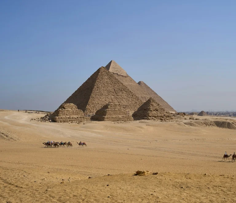 Camel caravan passing in front of the Giza pyramids, showing their massive scale - Pyramids Cairo tour