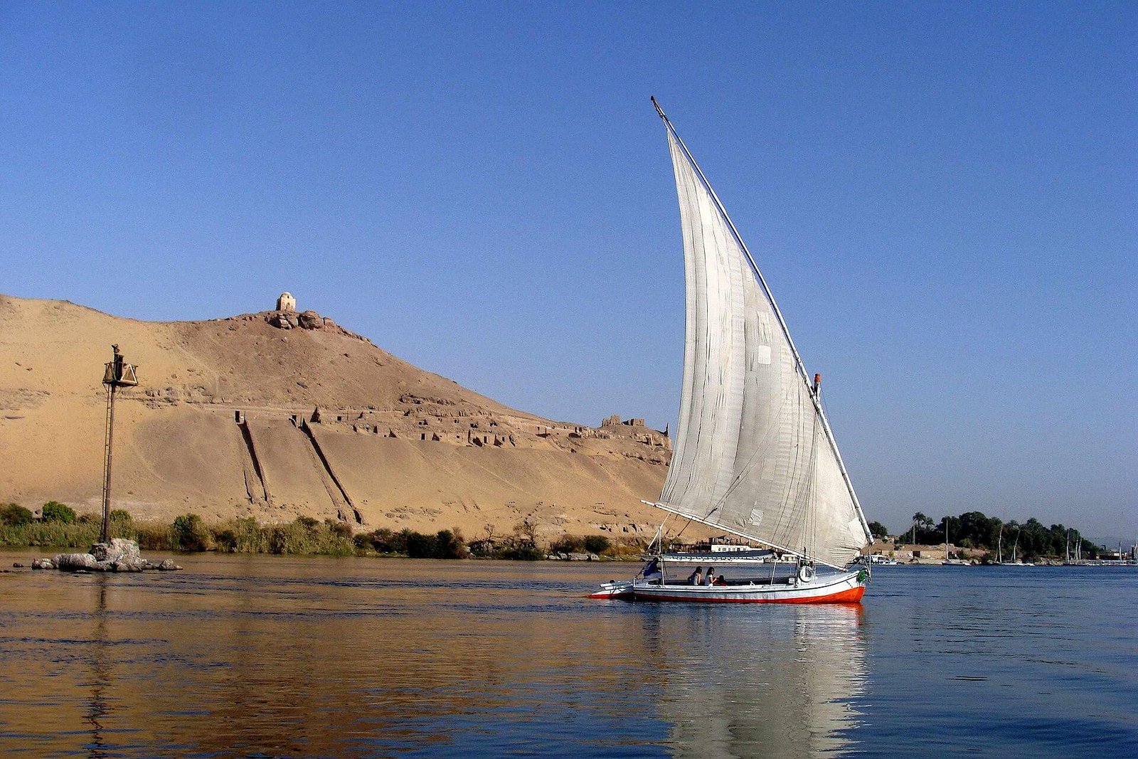 Qubbet el-Hawa domed summit above Aswan at sunset with a felucca on the Nile