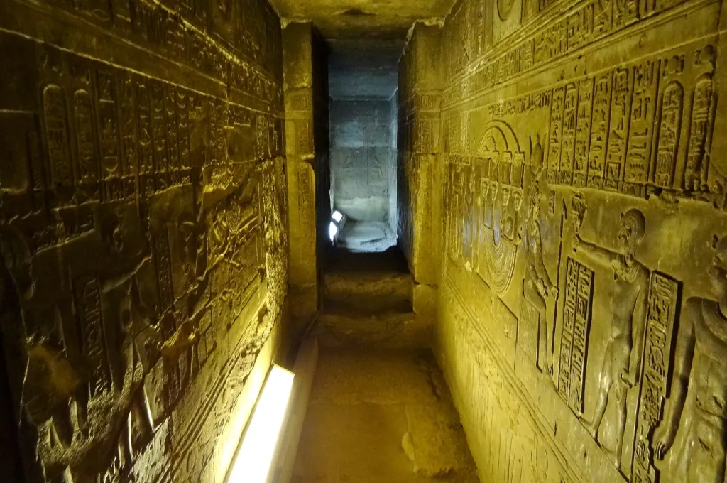 Narrow crypt corridor with carved walls beneath the Dendera temple lights relief