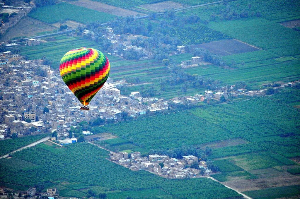 Hot air balloon ride price in Luxor: a balloon drifting above farmland at the edge of the desert